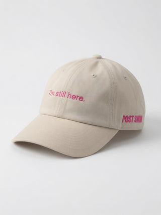 I'm Still Here Hat in stone with 'i'm still here.' embroidered in pink script and a pink POST SWIM logo on the side
