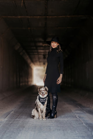 Melanoma survivor Amy Nichole in a black dress and hat, standing in a tunnel with her Australian Shepherd, Roxy