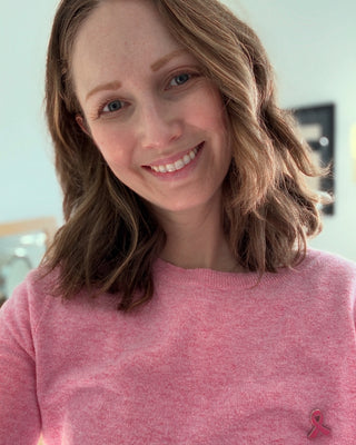 Woman wearing a pink sweater with a pink ribbon on a blurred indoor background