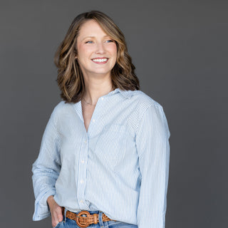 Woman wearing a light blue striped shirt and jeans against a gray background