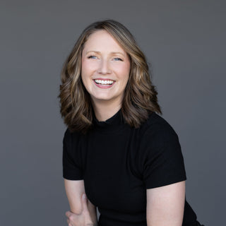 Woman in a black outfit sitting on a stool against a gray background