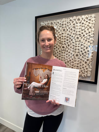 Person holding a magazine titled 'Glimmer of Hope' in front of a textured wall.