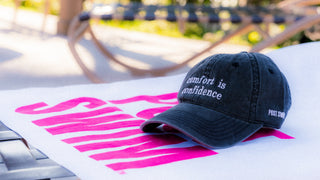 Black cap with text on a pink and white surface outdoors