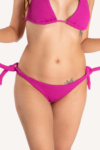 Front view of model wearing a magenta textured POST SWIM tie side bikini bottom with matching halter bikini top.