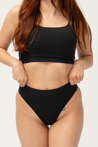 Front view of model wearing a POST SWIM black bikini set with bikini top and tummy control high waisted bikini bottom.