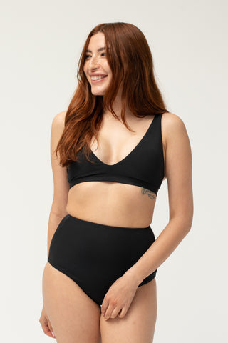 Front view of model wearing a POST SWIM black tummy control bikini bottom with matching bikini top.