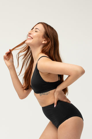 Side view of model wearing a POST SWIM black tummy control bikini bottom.